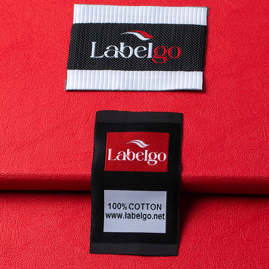 Primer plano de etiqueta tejida blanca y negra con el logotipo de LabelGo sobre fondo rojo.