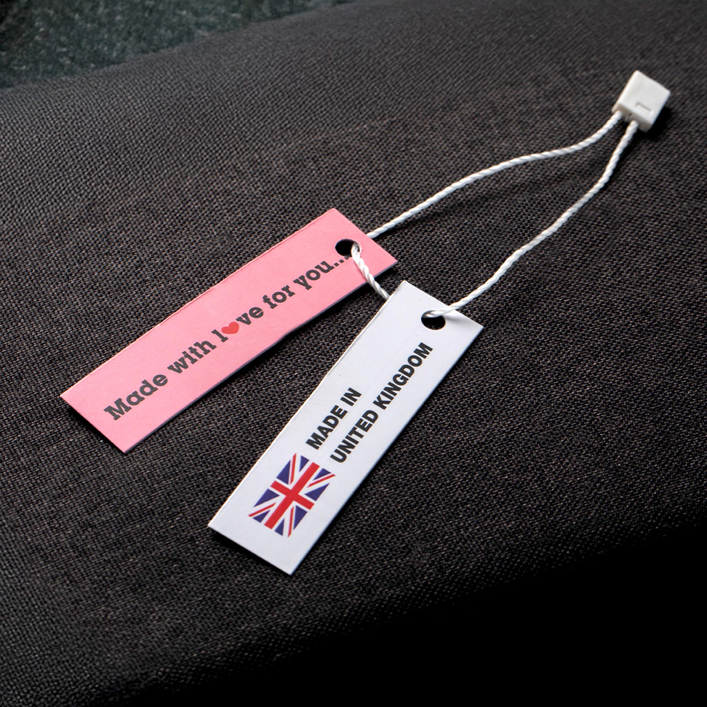 Etiqueta colgante de tela rosa con bordes deshilachados y cordel blanco de fijación.