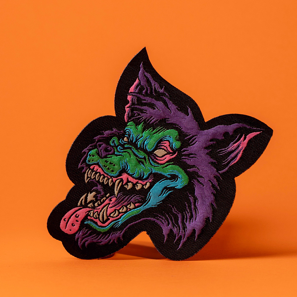 Parche bordado de lobo morado expuesto sobre un fondo naranja liso.