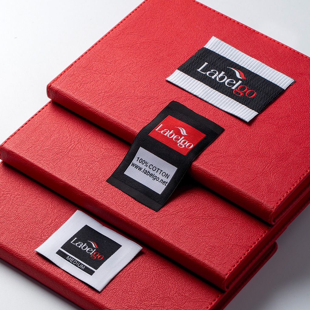 Etiquetas de ropa tejidas en jacquard colores negro y rojo presentadas sobre una caja roja.